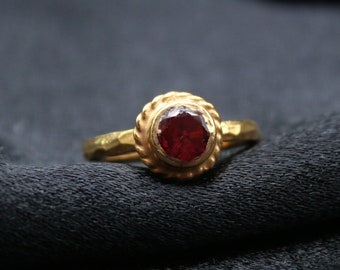 May include: A gold ring with a red gemstone set in a textured band.