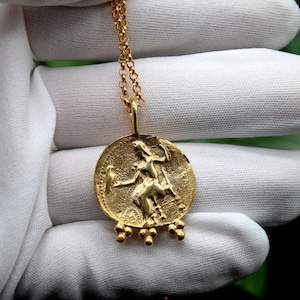 May include: A gold necklace with a round pendant featuring a detailed embossed image of a woman riding a horse. The pendant has a series of small gold beads hanging from the bottom.