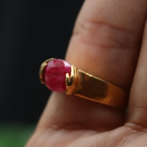 May include: A gold ring with a large, oval-shaped, red gemstone.