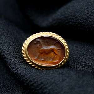 May include: A gold-toned oval ring with a brown cameo featuring a detailed carving of a lion.