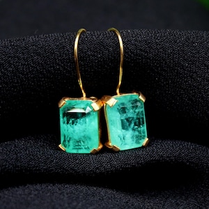 Peut inclure: Une paire de boucles d'oreilles en or avec des pierres précieuses vert émeraude. Les boucles d'oreilles ont un design simple et sont parfaites pour tous les jours.