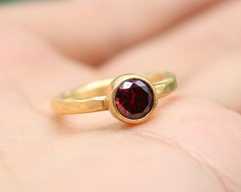 May include: A gold ring with a deep red gemstone set in a bezel setting.