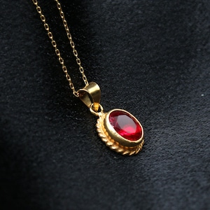 May include: A gold chain necklace with a red oval gemstone pendant.