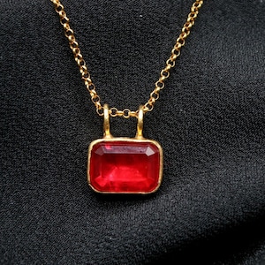 May include: A gold chain necklace with a red gemstone pendant. The pendant is a square shape with rounded corners.