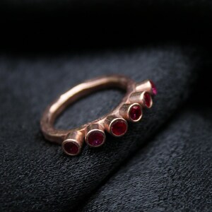 May include: A rose gold ring with a row of six red gemstones set in the band.