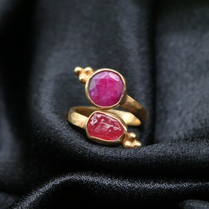 May include: A gold ring with two pink gemstones. The ring is designed to wrap around the finger.