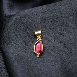 May include: A gold pendant featuring a red gemstone in the shape of a teardrop.