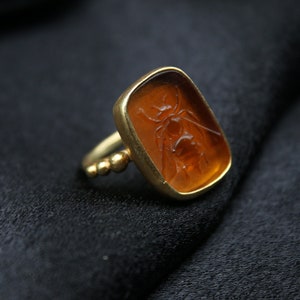 May include: A gold ring with a rectangular amber stone featuring a carved bee design.