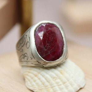 May include: A silver ring with an ornate design and a large, oval-shaped ruby gemstone.