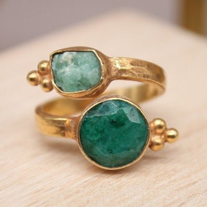 Peut inclure: Bague en or avec deux pierres d'émeraude vertes. La bague est une bande torsadée avec une petite émeraude d'un côté et une plus grosse émeraude ronde de l'autre.