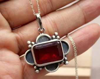 May include: A silver pendant necklace featuring a red gemstone set in a silver frame. The pendant is shaped like a four-leaf clover. The necklace is on a silver chain.