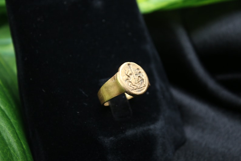 May include: A gold signet ring with a detailed engraved design. The ring has a rounded top and a smooth band.