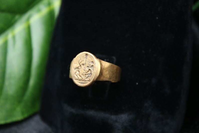 May include: A gold signet ring with a detailed engraved design of a mythical creature. The ring is set on a black velvet background.