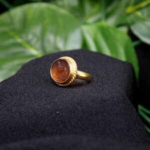 May include: A gold ring with a brown oval-shaped stone set in a gold bezel. The stone has a detailed carving on its surface.