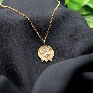 May include: A gold necklace with a round pendant featuring a detailed image of a woman. The pendant has three small gold beads hanging from the bottom.