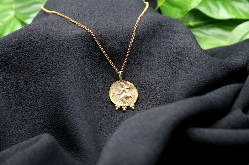 May include: A gold necklace with a round pendant featuring a detailed image of a woman. The pendant has three small gold beads hanging from the bottom.