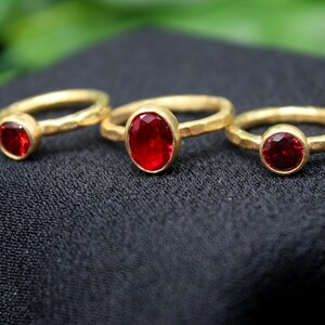 May include: Three gold rings with red gemstone settings. The rings are of different sizes and the gemstones are oval and round.