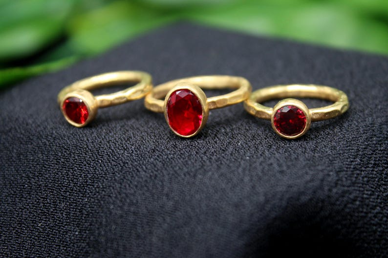 May include: Three gold rings with red gemstone settings. The rings are of different sizes and the gemstones are oval and round.
