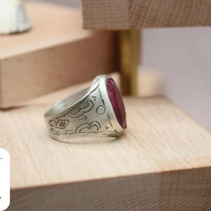 May include: A silver ring with an ornate design and a large, oval-shaped ruby gemstone.