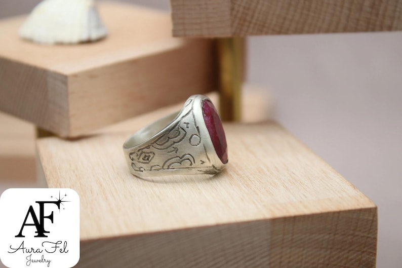May include: A silver ring with an ornate design and a large, oval-shaped ruby gemstone.