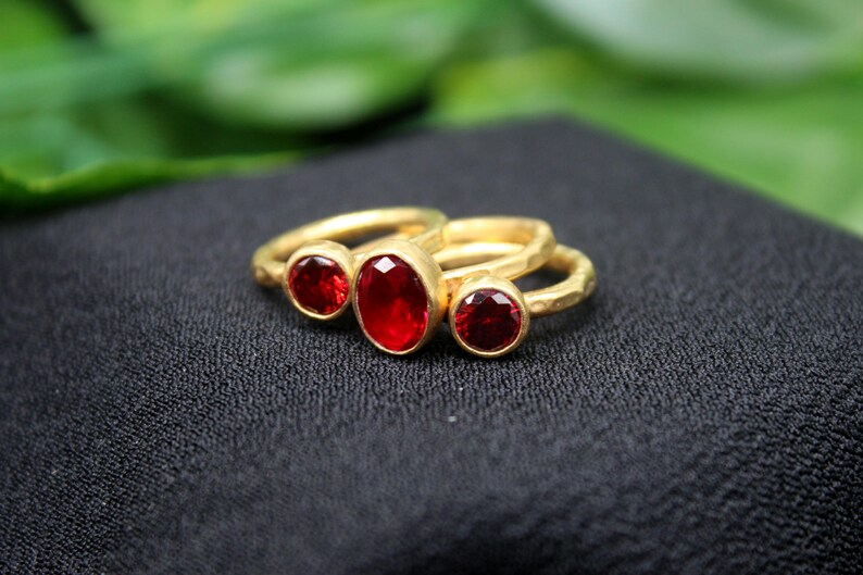 May include: Three gold rings with red oval-shaped gemstones. The rings are stacked on top of each other.