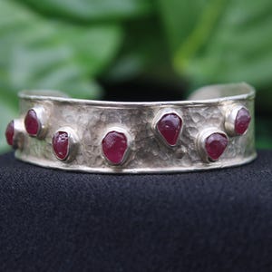 May include: A silver cuff bracelet with a hammered texture and eight pink gemstones set into the metal.
