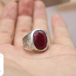 May include: A silver ring with an ornate design and a large, oval-shaped, red gemstone.