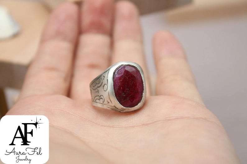 May include: A silver ring with an ornate design and a large, oval-shaped, red gemstone.