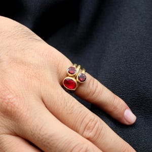 May include: A gold ring with three red gemstones. The ring is worn on a person's finger.