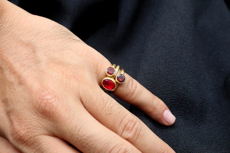 May include: A gold ring with three red gemstones. The ring is worn on a person's finger.
