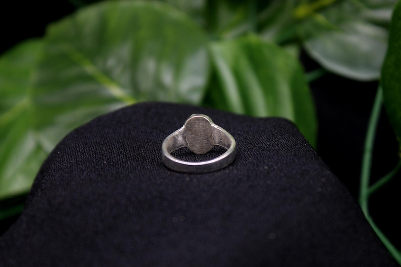 Pu&ograve; includere: Un anello d'argento con una parte superiore liscia di forma ovale. L'anello &egrave; su uno sfondo di tessuto nero.