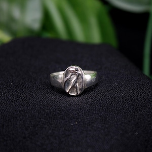 Pu&ograve; includere: Un anello d'argento con un design ovale che presenta un motivo testurizzato e astratto.