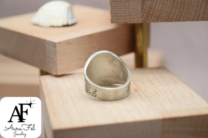 May include: A silver ring with a wide band and a smooth, rounded top. The ring is sitting on a wooden surface.