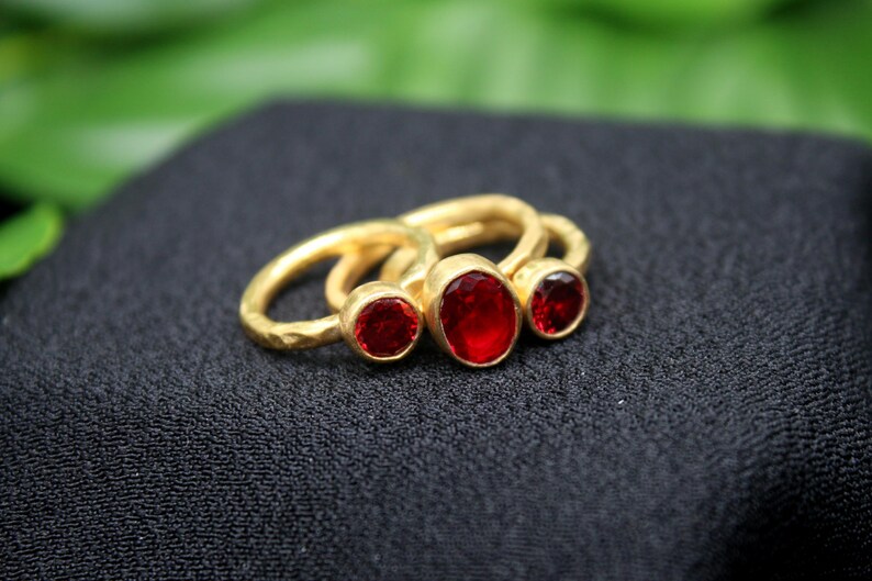 May include: Three gold rings with red gemstones. The rings are stacked on top of each other. The largest ring has a large oval-shaped red gemstone. The middle ring has a smaller round red gemstone. The smallest ring has a small round red gemstone.