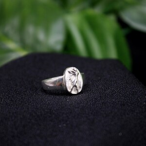 Pu&ograve; includere: Un anello d'argento con un design ovale che presenta un motivo floreale stilizzato.