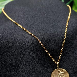 May include: A gold chain necklace with a round pendant featuring a detailed design. The pendant is hanging from a delicate chain.