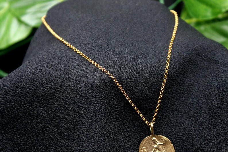 May include: A gold chain necklace with a round pendant featuring a detailed design. The pendant is hanging from a delicate chain.