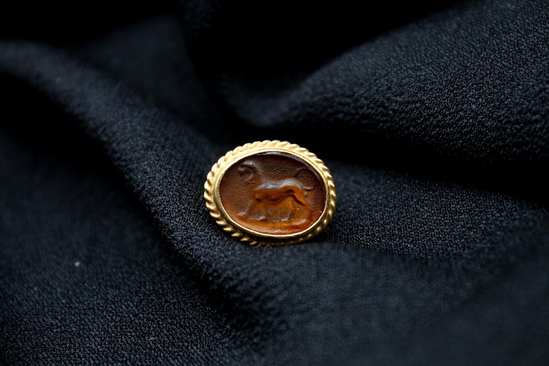 May include: A gold-toned oval ring with a brown cameo featuring a detailed carving of a lion.