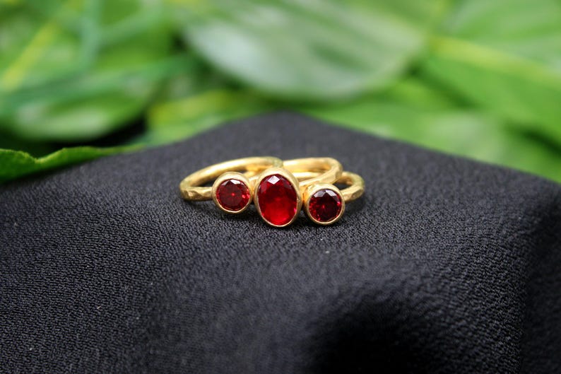 May include: Gold ring with three red gemstones. The center stone is oval shaped and the two side stones are round.