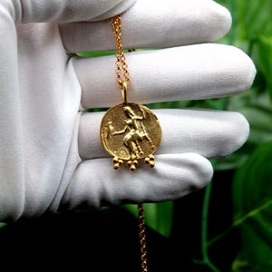 May include: A gold necklace with a round pendant featuring a detailed relief of a woman riding a horse. The pendant has five small gold beads hanging from the bottom.