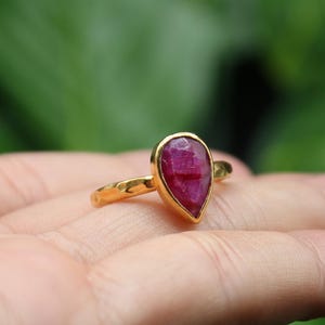 May include: A gold ring with a teardrop-shaped ruby gemstone. The ring has a textured band.