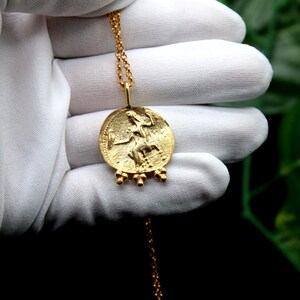 May include: A gold necklace with a round pendant featuring a detailed image of a woman. The pendant has a textured surface and is accented with small gold beads.