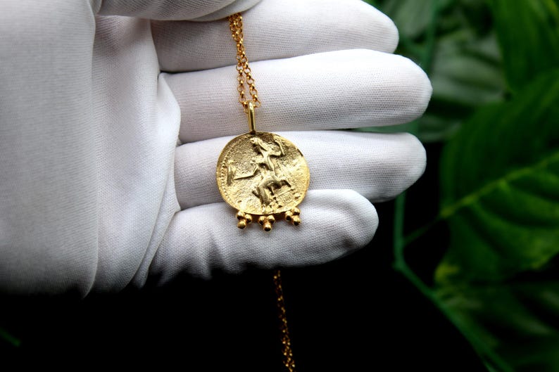 May include: A gold necklace with a round pendant featuring a detailed image of a woman. The pendant has a textured surface and is accented with small gold beads.