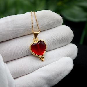 Könnte beinhalten: Eine goldene Kettenkette mit einem roten Herz-Anhänger. Das Herz ist aus Glas und hat einen goldenen Rand.