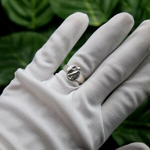 Pu&ograve; includere: Un anello d'argento con un design ovale testurizzato. L'anello &egrave; su una mano guantata di bianco.