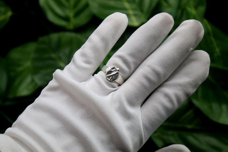 Pu&ograve; includere: Un anello d'argento con un design ovale testurizzato. L'anello &egrave; su una mano guantata di bianco.