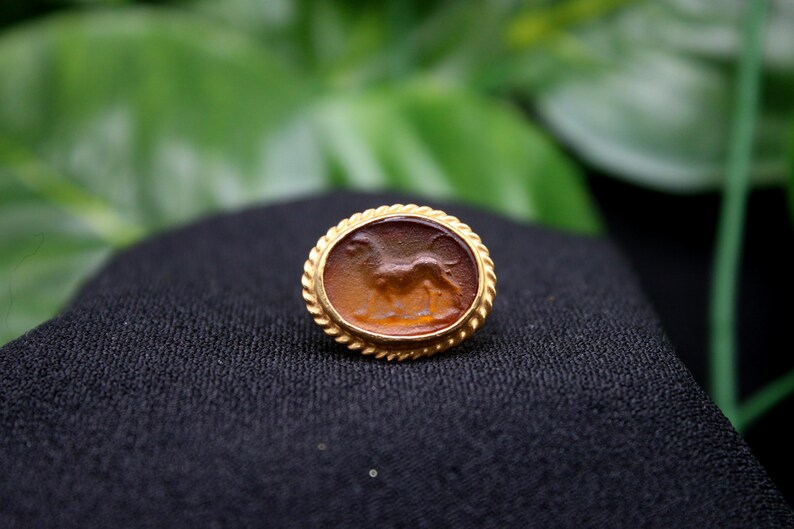 May include: A gold-toned ring with a brown cameo featuring a carved image of a lion.