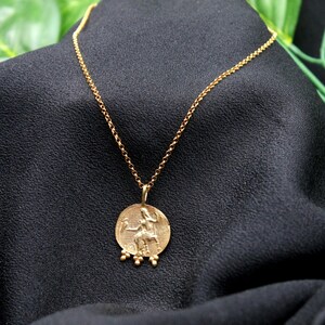 May include: A gold chain necklace with a round pendant featuring a detailed image of a person riding a horse. The pendant has small beads around the edge.