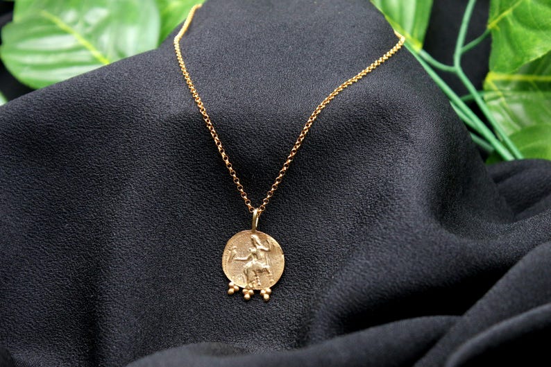 May include: A gold chain necklace with a round pendant featuring a detailed image of a person riding a horse. The pendant has small beads around the edge.