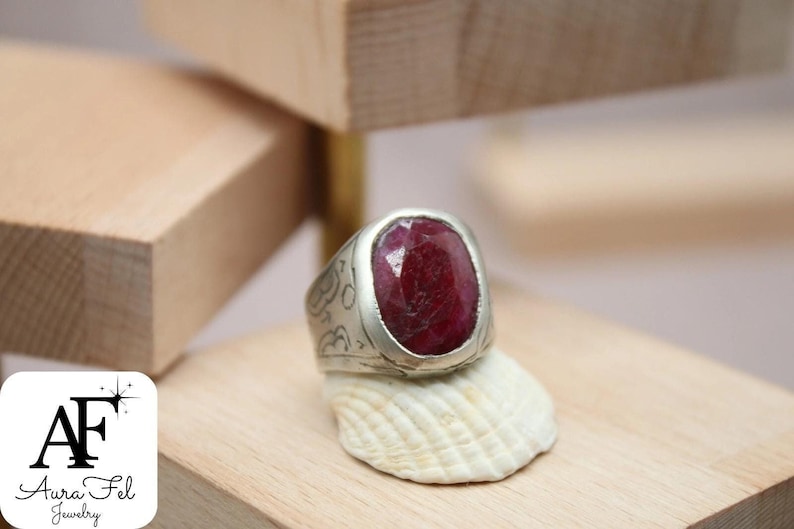 May include: A silver ring with an ornate design and a large, oval-shaped ruby gemstone.